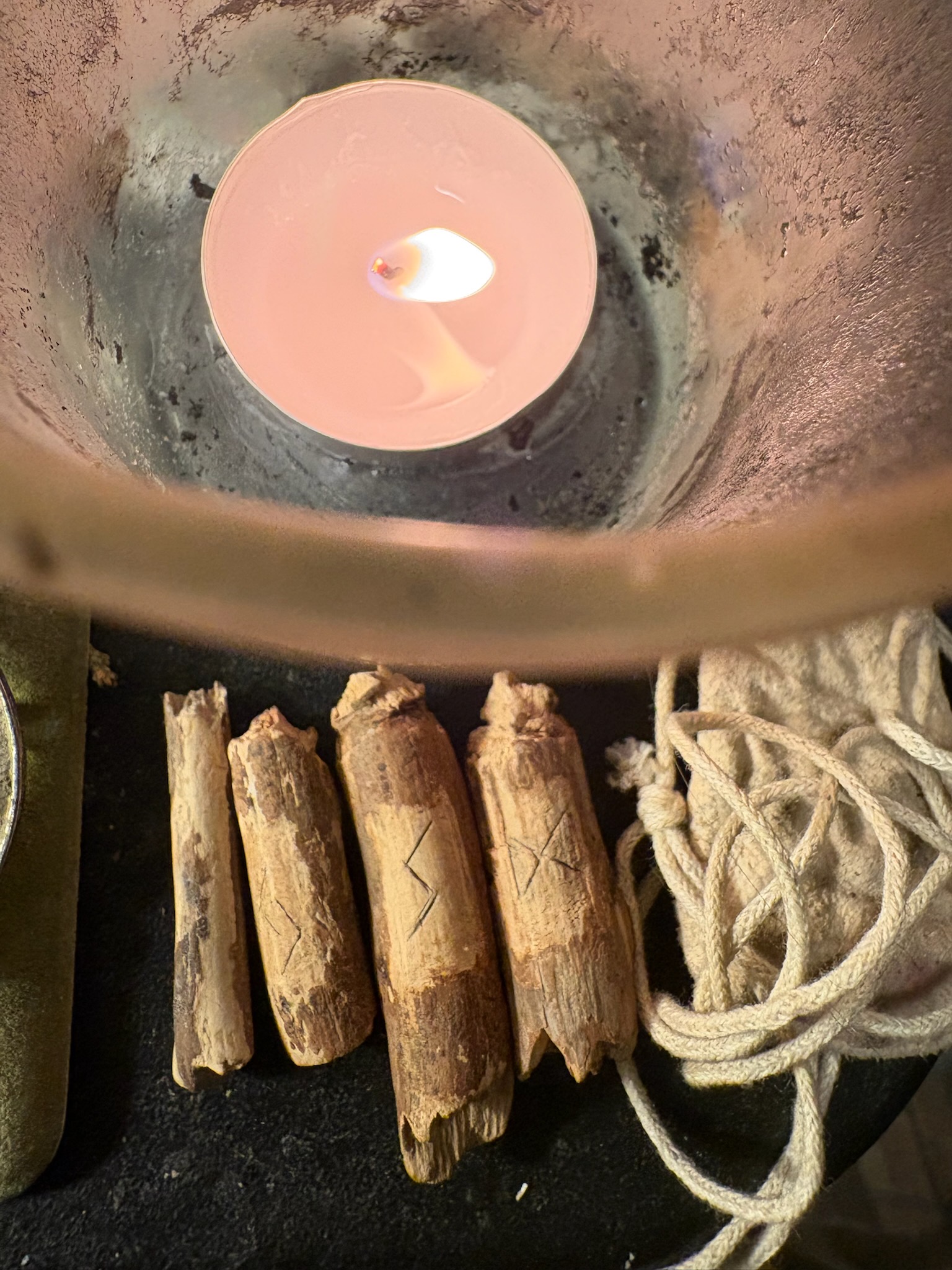 Shamanic rune ritual altar with hand-carved wooden rune staves and lit candle in a copper bowl after completing a summer solstice rune ceremony